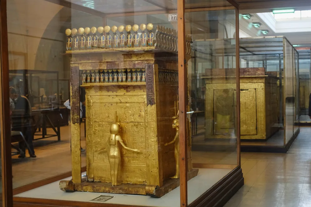 A gilded shrine topped with cobras stands in a glass case, guarded by a gold goddess with outstretched arms.