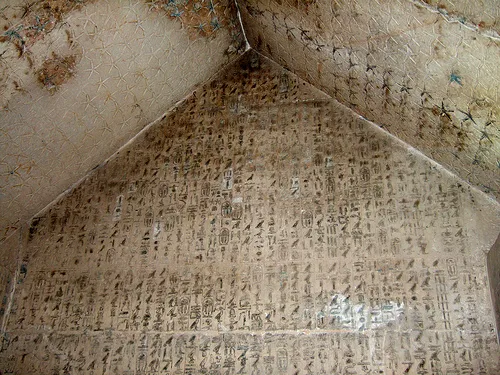Columns of carved hieroglyphs cover a gabled burial chamber wall below a ceiling painted with stars.