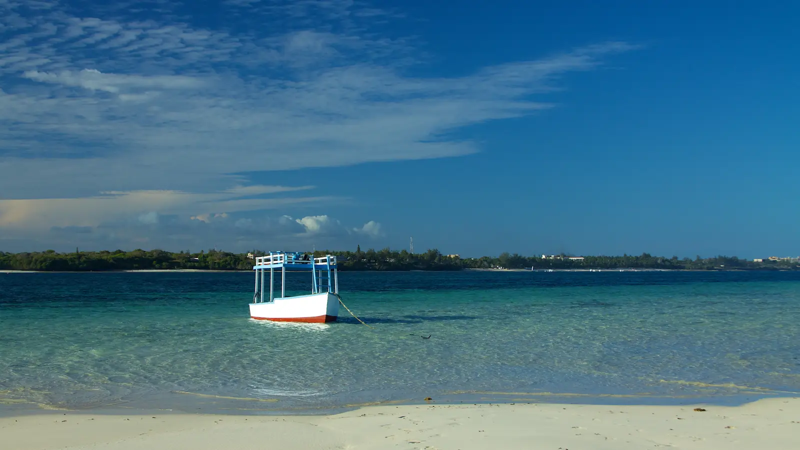A small white boat sits on clear turquoise water beyond a bank of white sand.