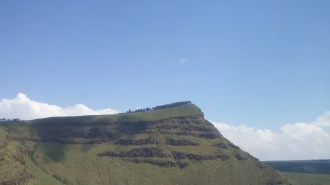 A green escarpment with banded rock terraces runs along the edge of a caldera.