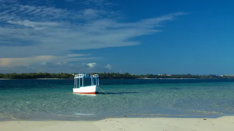 A small white boat sits on clear turquoise water beyond a bank of white sand.